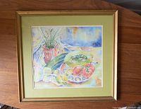 Full view of framed watercolour painting showing fruit and chives still life on table with gold-toned frame and green mat board