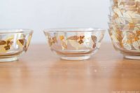 Close-up of two small glass bowls showing detailed gold and white leaf motifs on the clear glass.