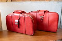 Pair of red vintage suitcases showing their full front and side profile on a wooden surface.