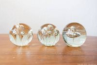 Three clear glass round paperweights with internal bubble shapes displayed on wooden surface