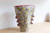 Full view photo showing the cone-shaped vase with textured floral patterns and multiple red ceramic loops on sides.