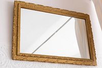 Front angled view of the gold painted ornate framed mirror hung on wall, showing the entire mirror and decorative details.