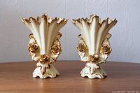 Pair of Art Nouveau style vases with cream finish and gold accents featuring floral motifs, shown front-facing with scalloped edges.