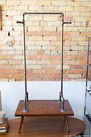 Full view of clothing rack showing metal piping frame and wooden table base against brick wall.