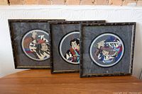 Set of three framed circular Asian hook rugs in bamboo style wood frames on wood table.