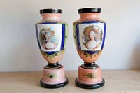 Pair of pink painted milk glass vases or urns with black, gold, blue, and green highlights, each depicting a woman in Regency style clothing on one side.