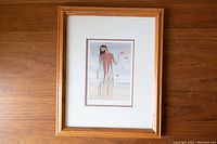 Overall front view of framed print on wooden floor, showing light wood frame and matted art.