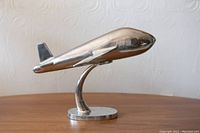 Side view of a sleek pewter decorative airplane sculpture mounted on its stand, showing the smooth metallic surface and oval base.