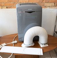 AC unit with exhaust hose and window panel components on wooden table