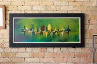 Full front view of framed cityscape painting in green and multiple colors on an exposed brick wall.