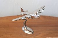 Front angled view of a pewter airplane sculpture showing four propellers and smooth finish, placed on wooden surface.