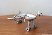 Front angle view of the pewter decorative airplane showing propellers and wheels resting on a wooden surface.