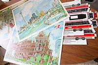 Three Toronto landmark prints laid flat showing colorful artistic depictions of Casa Loma, Old City Hall, and the Toronto skyline, with a nearby flat TTC streetcar cutout.