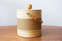 Front view of the vintage faux wicker plastic ice bucket with lid and knob on wooden table with handle down.