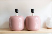Pair of pink ceramic vintage Ikea lamps on wooden shelf, no bulbs or shades, rounded square shapes with black lamp sockets.
