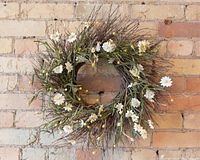 Full front view of the vintage twig wreath against brick wall, showing white and yellow artificial flowers scattered throughout.