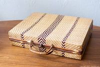 Top front angle view showing woven beige wicker, dark brown geometric stripe patterns, and wicker-wrapped handle attached to wooden rod frame.