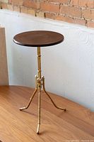Full view of the vintage side table with round wood top and brass tripod legs.