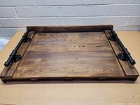 Top-down angled view of rectangular wooden serving tray with visible wood grain and pipe handles on each side.