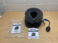Photo of Branfit neck traction device inflated, showing the collar shape with connected pump, instruction manual and packaging.