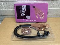 Manicure training practice hand with flexible fingers attached to black adjustable clamp mount, box in background indicates inclusion of 100 tips