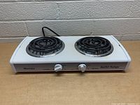 Front angle view of white Munsey buffet range with two coil burners and control knobs against a brick wall.