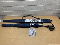 New Sport-Brella clamp-on umbrella folded next to its navy blue carrying case and instruction manual on a wooden surface.
