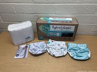 Photo of three reusable printed cloth diapers, 25 disposable inserts next to box in background