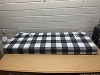 Top view of the rectangular cushion on a wooden table showing its checkered black and white fabric and securing ties.