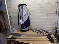 Set of Ultra women's golf clubs laid out on table with golf bag standing behind.