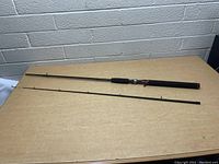 Full view of the two pieces of the Shakespeare Ugly Stik GX2 fishing pole laid flat on a tabletop, showing the foam handle and rod guides.