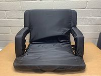 Front view of the black wide portable stadium seat with padded armrests and backrest showing the seating area.