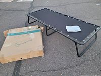 Fold away bed laid out flat next to damaged cardboard box packaging and instruction manual.