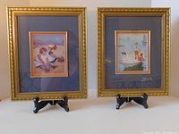 Front view of two double framed prints on display stands showing impressionist beach scenes.