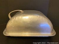 Closed view of antique aluminum roasting pan with dome lid and handle, showing surface wear and dents.