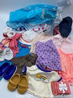 Top view of assorted doll clothing including dresses and tops in various colors and fabrics laid out on the floor