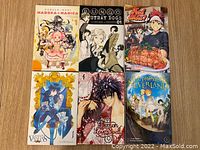 Front view of six manga books arranged in two rows of three. Covers visible show colorful anime/manga characters from titles including Madoka Magica, Bungo Stray Dogs, Food Wars, The Case Study of Vanitas, Demon Love Spell, and The Promised Neverland.