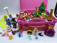 Playmobil figures and assorted accessories inside and around two pink carrying cases, showing full assortment and storage cases.
