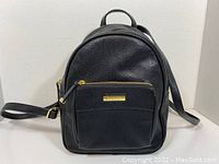 Front view of the black Calvin Klein backpack showing front zippered pocket with gold-tone zipper and logo plate.
