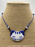 Front close-up photo of the blue and white ceramic sleeping cat face pendant necklace on display, showing detail on the cat face and blue adjustable cord.