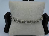 Full view of the silver tone heavy curb chain link bracelet displayed on a white cushion, showing the chain thickness and length.