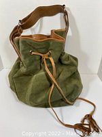 Green suede drawstring purse with tan leather strap and trim, shown upright.