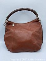 Front view of the medium brown leather purse with dark brown braided leather handle clipped on. The leather has a smooth, slightly textured finish.