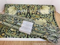 Overview showing three sealed rolls and one open roll of wallpaper against black background with green and cream floral pattern