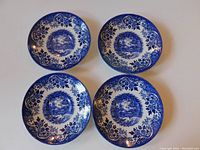 Four Broadhurst Ironstone saucers in a dark blue and white pattern depicting an English countryside and lake scene, arranged flat on a surface.