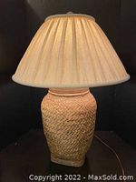 Front view of the vintage table lamp showing woven basket base and pleated fabric shade illuminated.