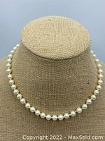 Front view of the vintage knotted white pearl necklace displayed on a beige fabric bust showing lustrous round pearls.