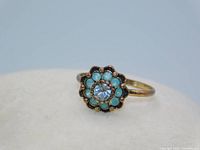 Front angle photo showing clear central rhinestone and surrounding pale green rhinestones in flower pattern on gold-tone band.