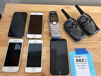 Full lot showing six iPhones, one Linksys phone, and a pair of black walkie-talkies on a wooden surface