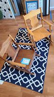 Two small wooden rocking chairs positioned on a geometric-patterned throw rug; one chair upright, one upside down showing broken armrest.